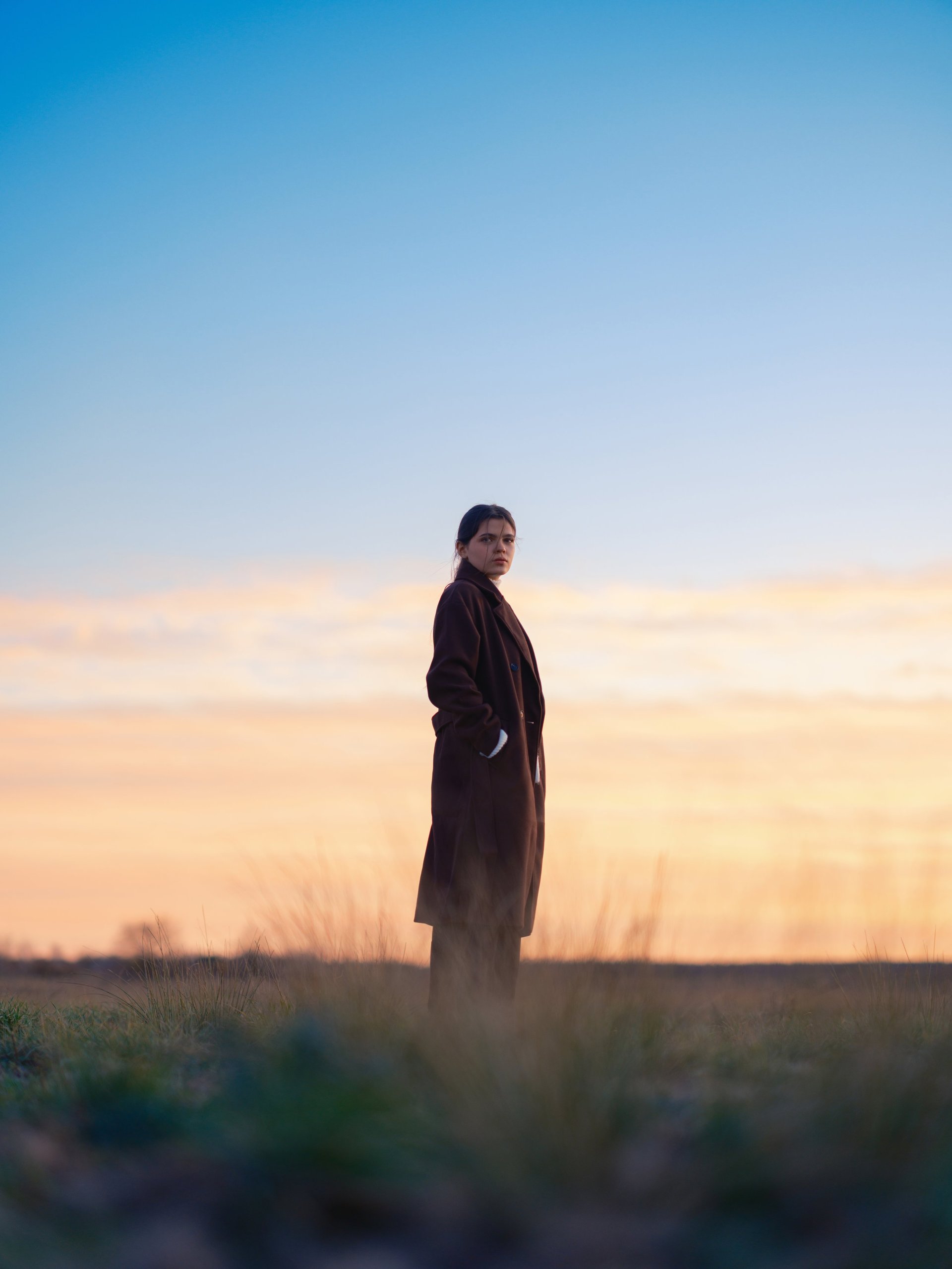 Low angle portrait of a woman standing in silhouette against a golden hour sky, calm and present